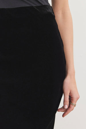 Close-up of a person wearing the EZA SILK VELVET SKIRT by Velvet by Graham & Spencer, showing their right hand with a gold ring, resting by their side.