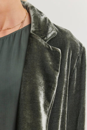 Close-up of a person wearing the KYLA SILK VELVET BLAZER by Velvet by Graham & Spencer, showcasing an oversized fit and notched collar, layered over a matching blouse with a delicate gold necklace.