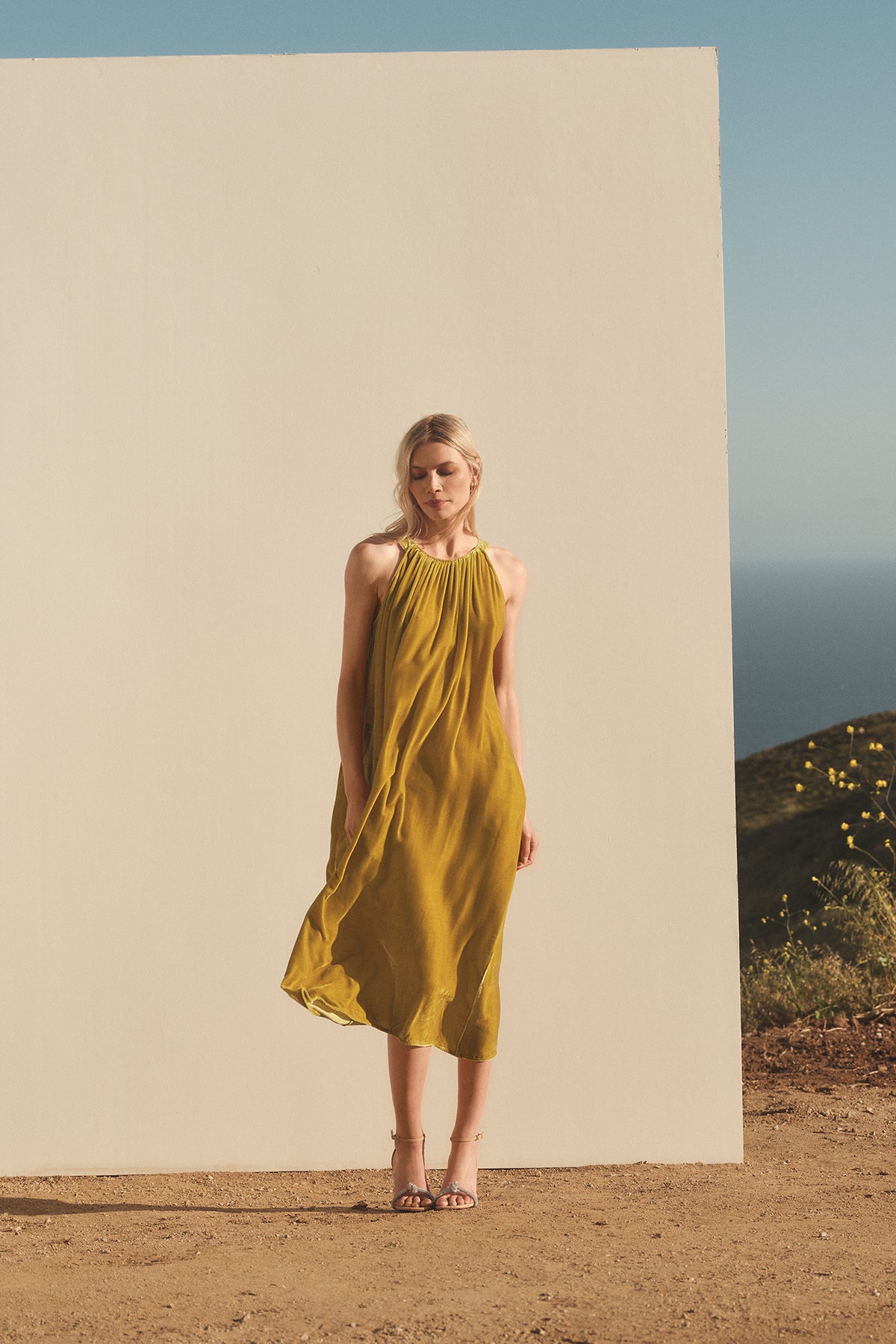 A woman in a MAREN SILK VELVET HALTER DRESS by Velvet by Graham & Spencer standing in front of a white wall.-35571948880065