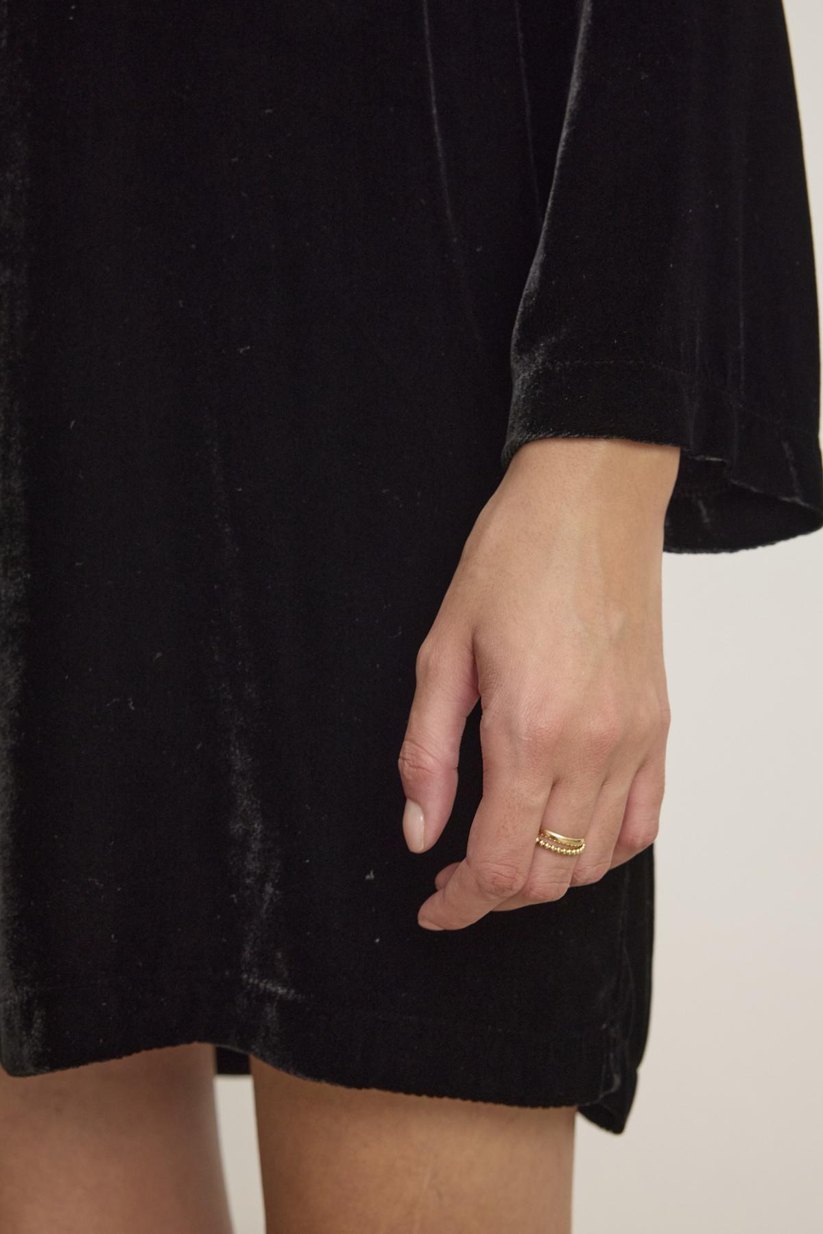 A hand adorned with a gold ring rests elegantly against the luxurious SHERI SILK VELVET DRESS by Velvet by Graham & Spencer.