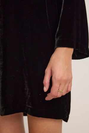A hand adorned with a gold ring rests elegantly against the luxurious SHERI SILK VELVET DRESS by Velvet by Graham & Spencer.
