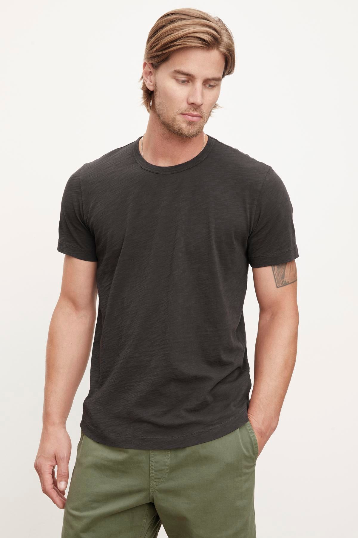   A man with blond hair wearing a Velvet by Graham & Spencer AMARO TEE and olive green pants, standing against a plain background. 