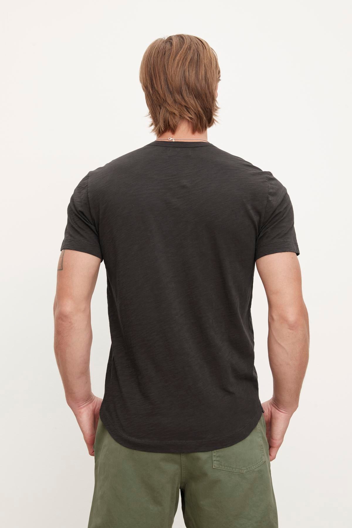   Rear view of a man with brown hair wearing a Velvet by Graham & Spencer AMARO TEE crew neck t-shirt and olive green pants, standing against a plain background. 