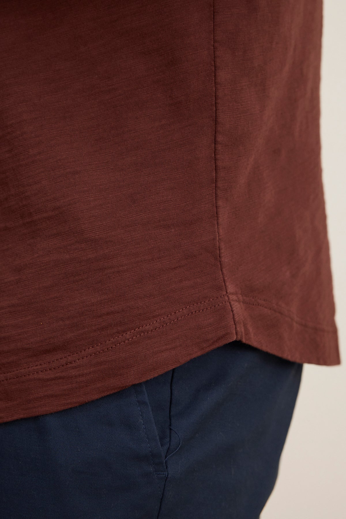 A close-up of the lower side of the AMARO TEE by Velvet by Graham & Spencer in brown Peruvian cotton with a crew neckline, styled with dark blue pants—a versatile layering piece for any wardrobe.