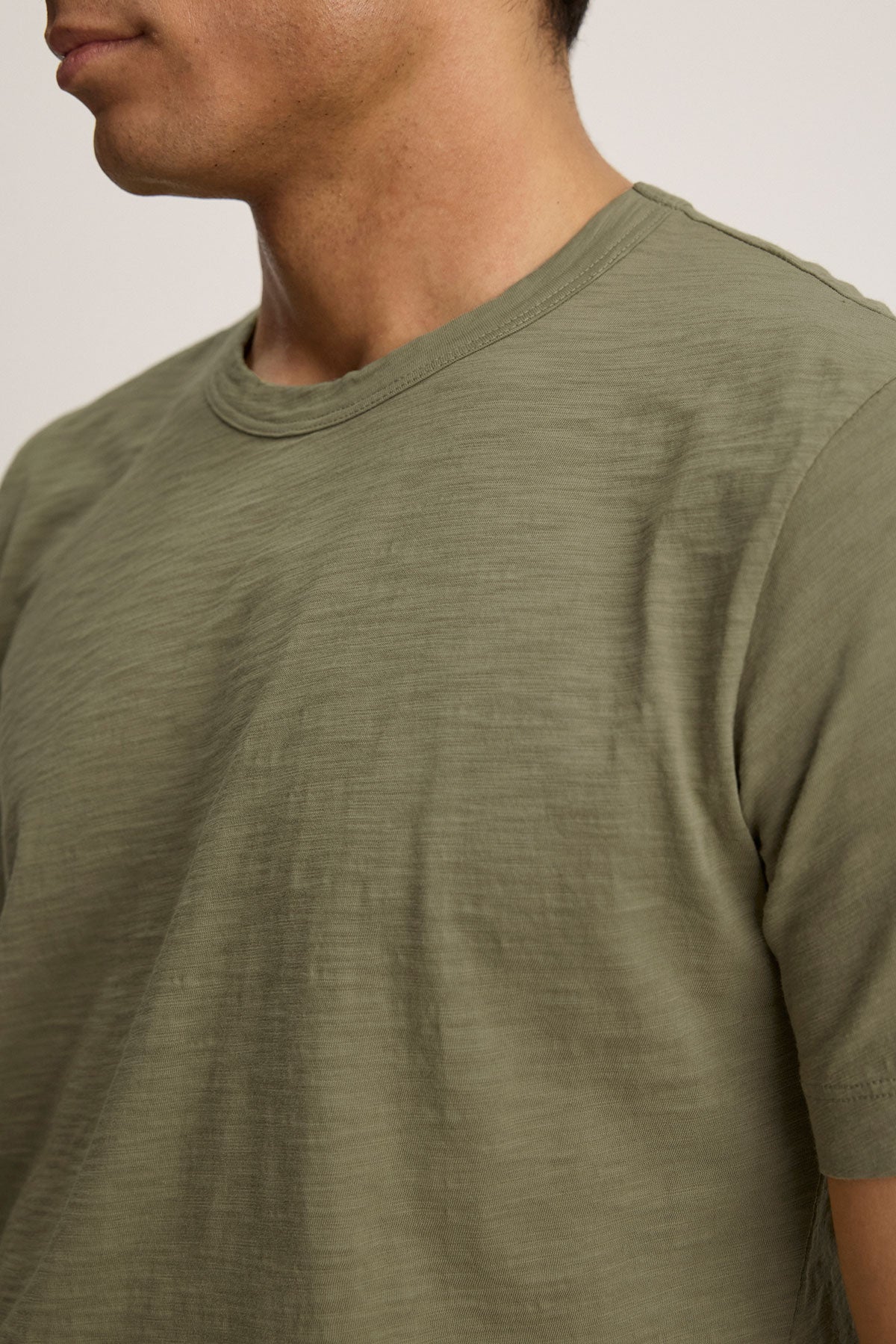 A person wears the AMARO TEE by Velvet by Graham & Spencer—light olive green, short-sleeve Peruvian cotton crewneck—shown from shoulders to mid-chest, facing slightly left; an ideal layering piece for everyday comfort.-40117505327297