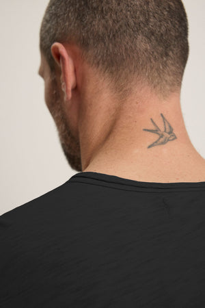 A person with a bird tattoo on their neck is seen from the back, wearing a classic crew neckline black CHAD TEE made from soft Peruvian cotton by Velvet by Graham & Spencer.
