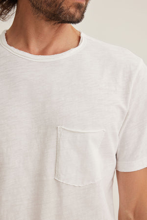 A person wearing the CHAD TEE by Velvet by Graham & Spencer, featuring a classic crew neckline and raw edge details, has a front pocket and their face is partially visible.