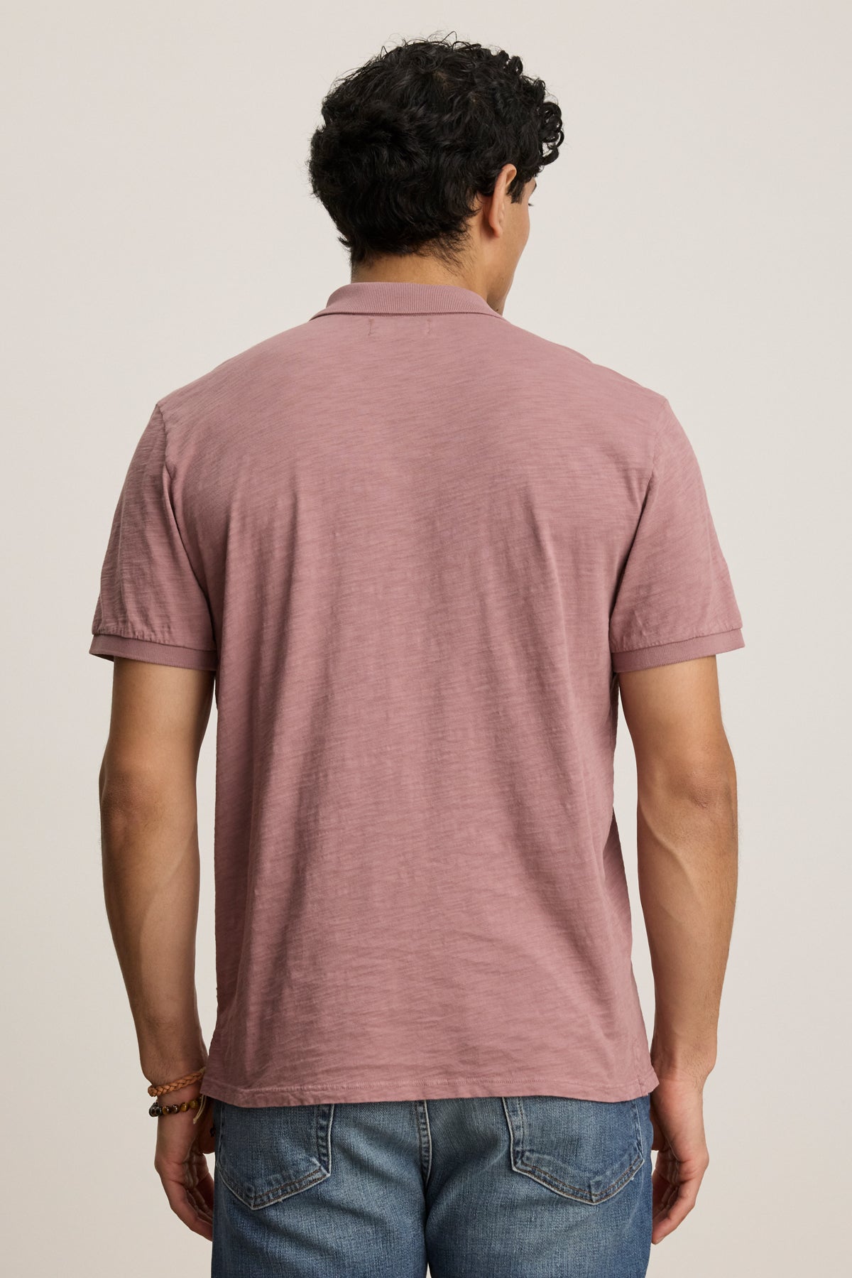A man faces away from the camera, wearing the NIKO POLO by Velvet by Graham & Spencer—crafted from Peruvian cotton—paired with blue jeans, set against a plain background.-40054347268289