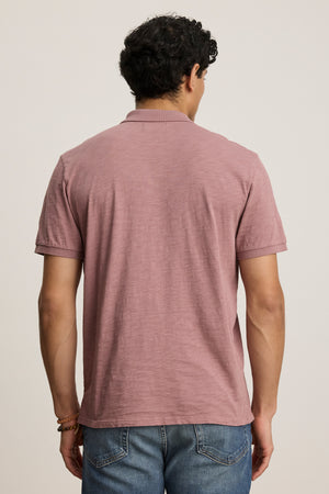 A man faces away from the camera, wearing the NIKO POLO by Velvet by Graham & Spencer—crafted from Peruvian cotton—paired with blue jeans, set against a plain background.