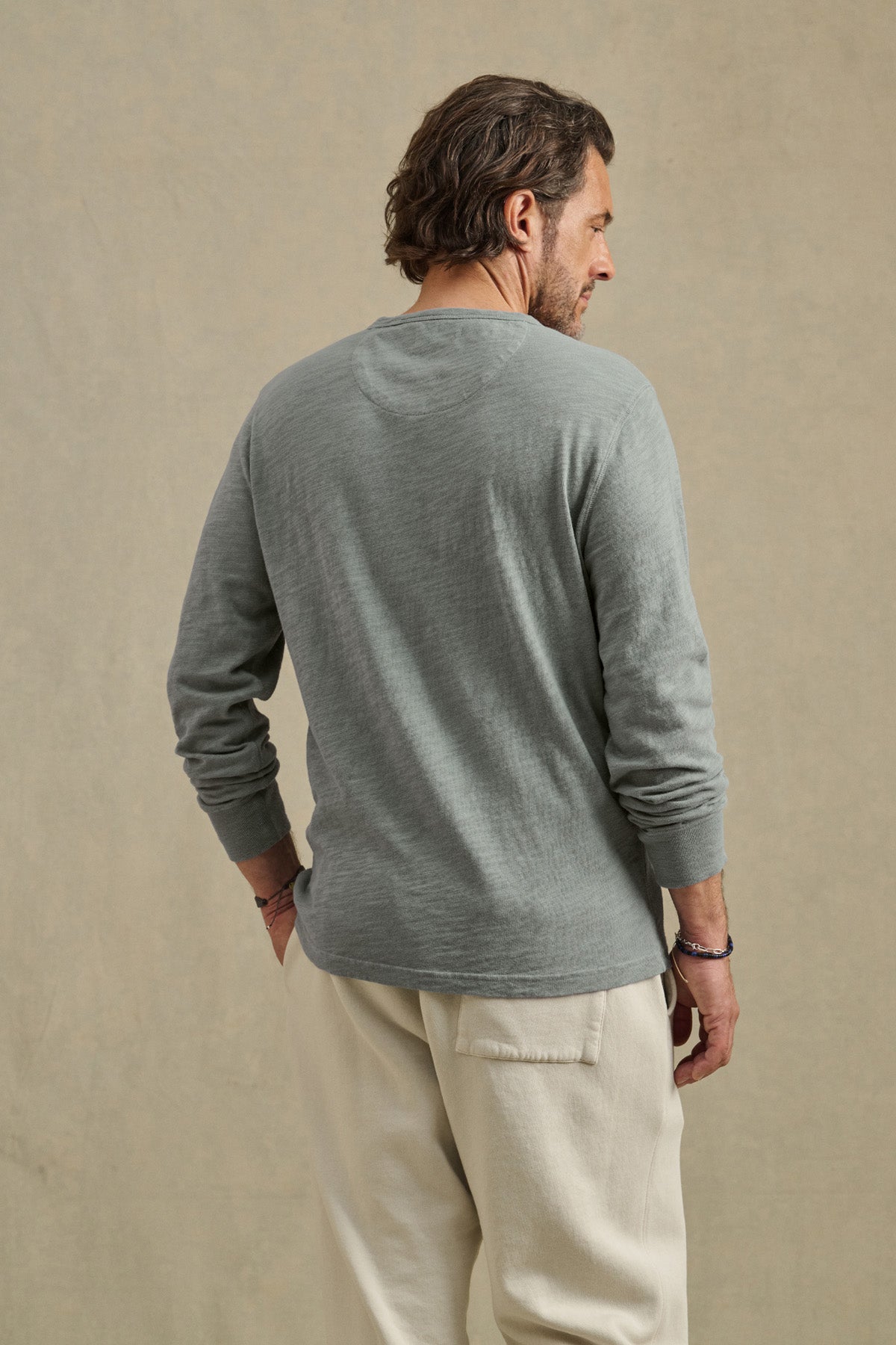 A man wearing the DUSTIN TEE by Velvet by Graham & Spencer and beige pants stands facing away against a plain beige background.-41145260933313