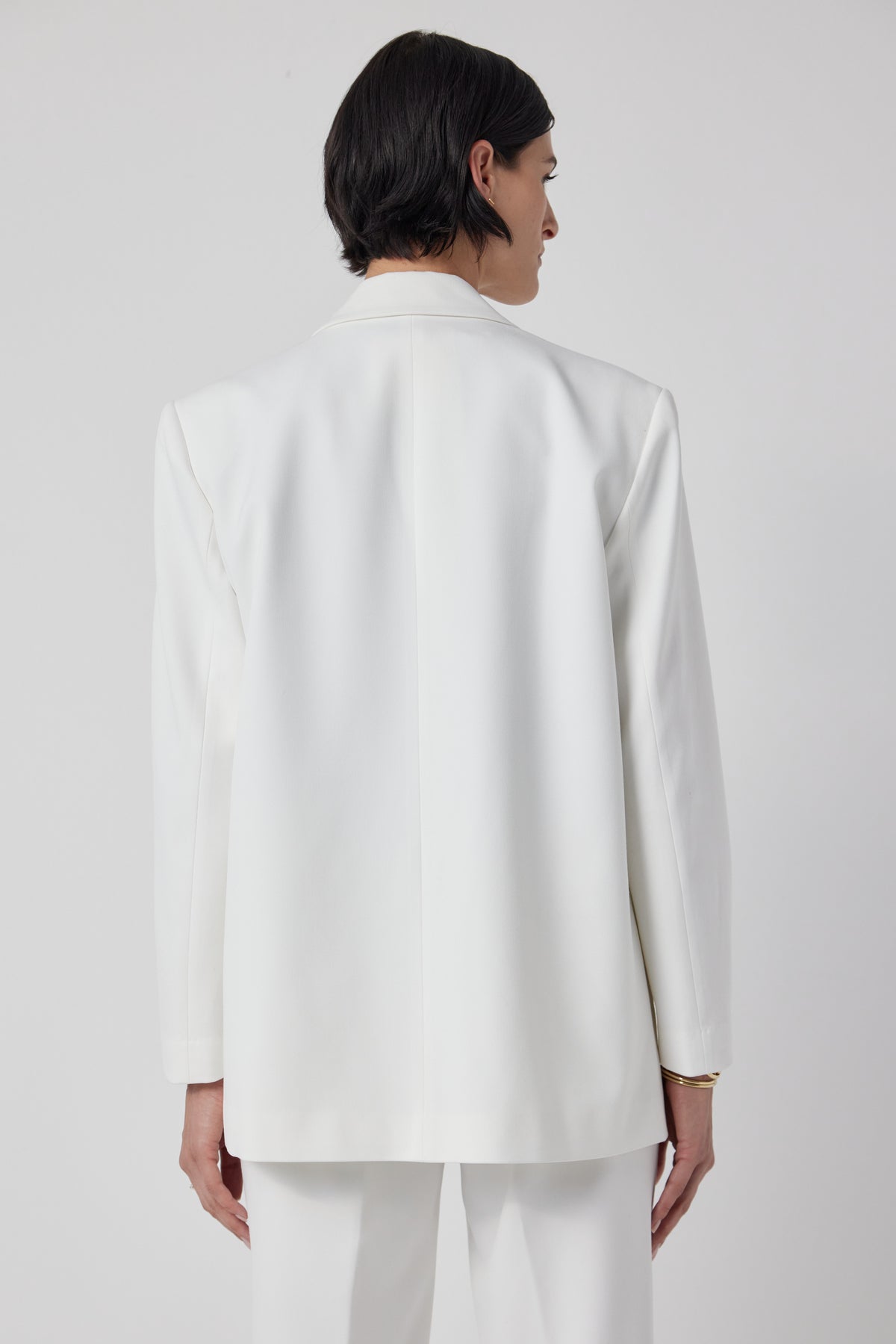  The back view of a woman wearing a structured white Fairfax blazer and pants by Velvet by Jenny Graham. 