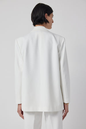 The back view of a woman wearing a structured white Fairfax blazer and pants by Velvet by Jenny Graham.