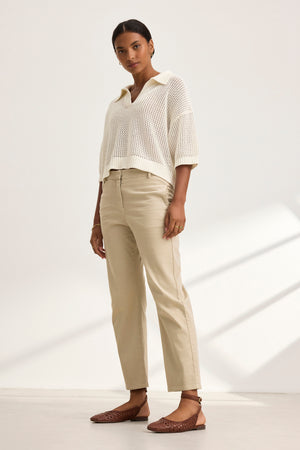 In a neutral-toned room, a person dons a white knit sweater, the