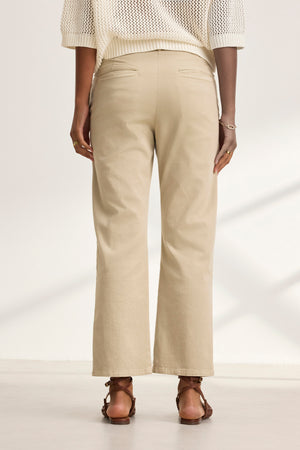 An individual in a cream sweater and Velvet by Graham & Spencer's MUSE PANT in beige, facing away. Brown sandals and a bracelet are noticeable.
