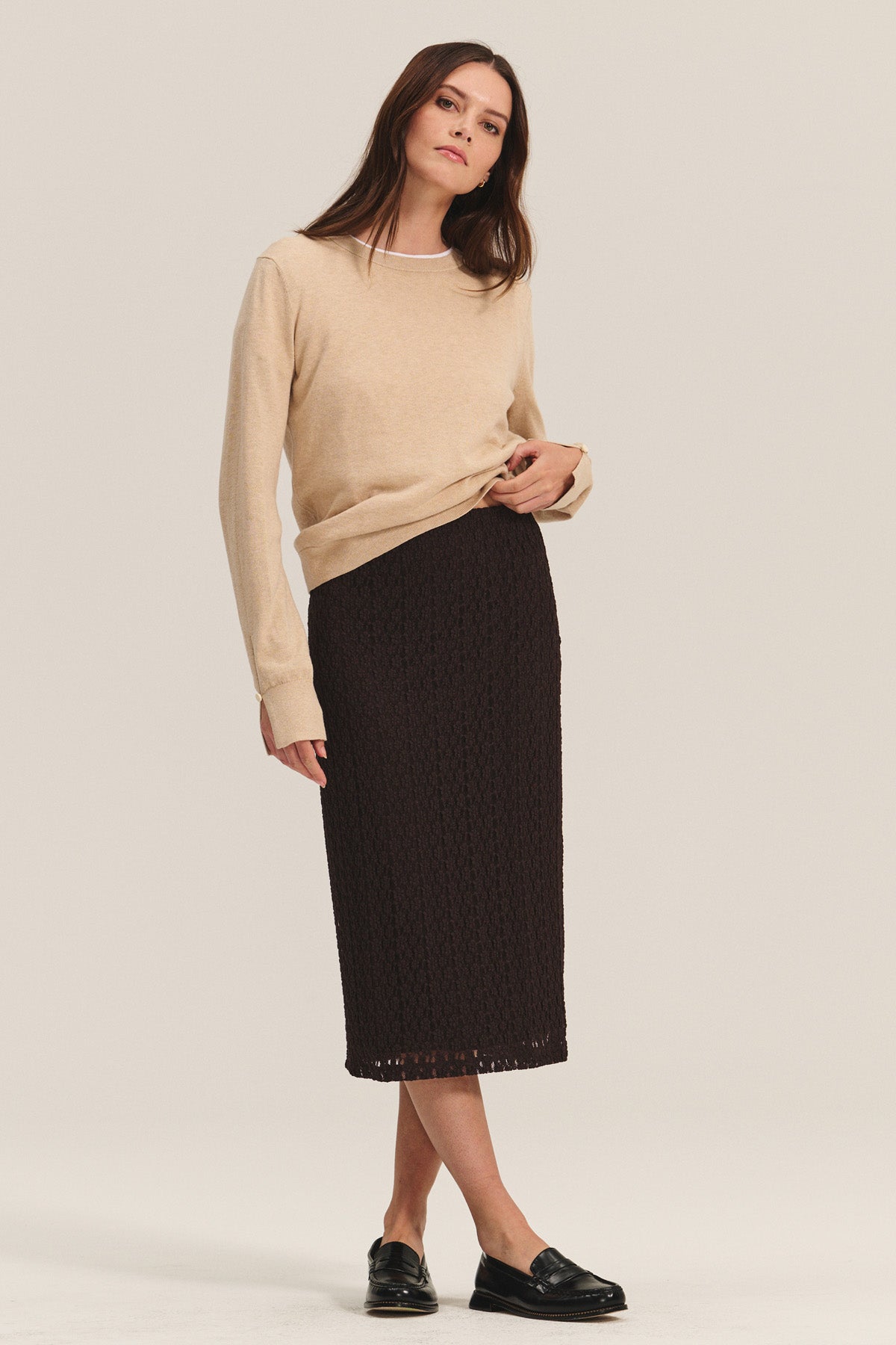 A woman wears the MELINA SWEATER by Velvet by Graham & Spencer—beige with ribbed trims—paired with a black textured midi skirt and black loafers, standing against a plain background.-40681731424449