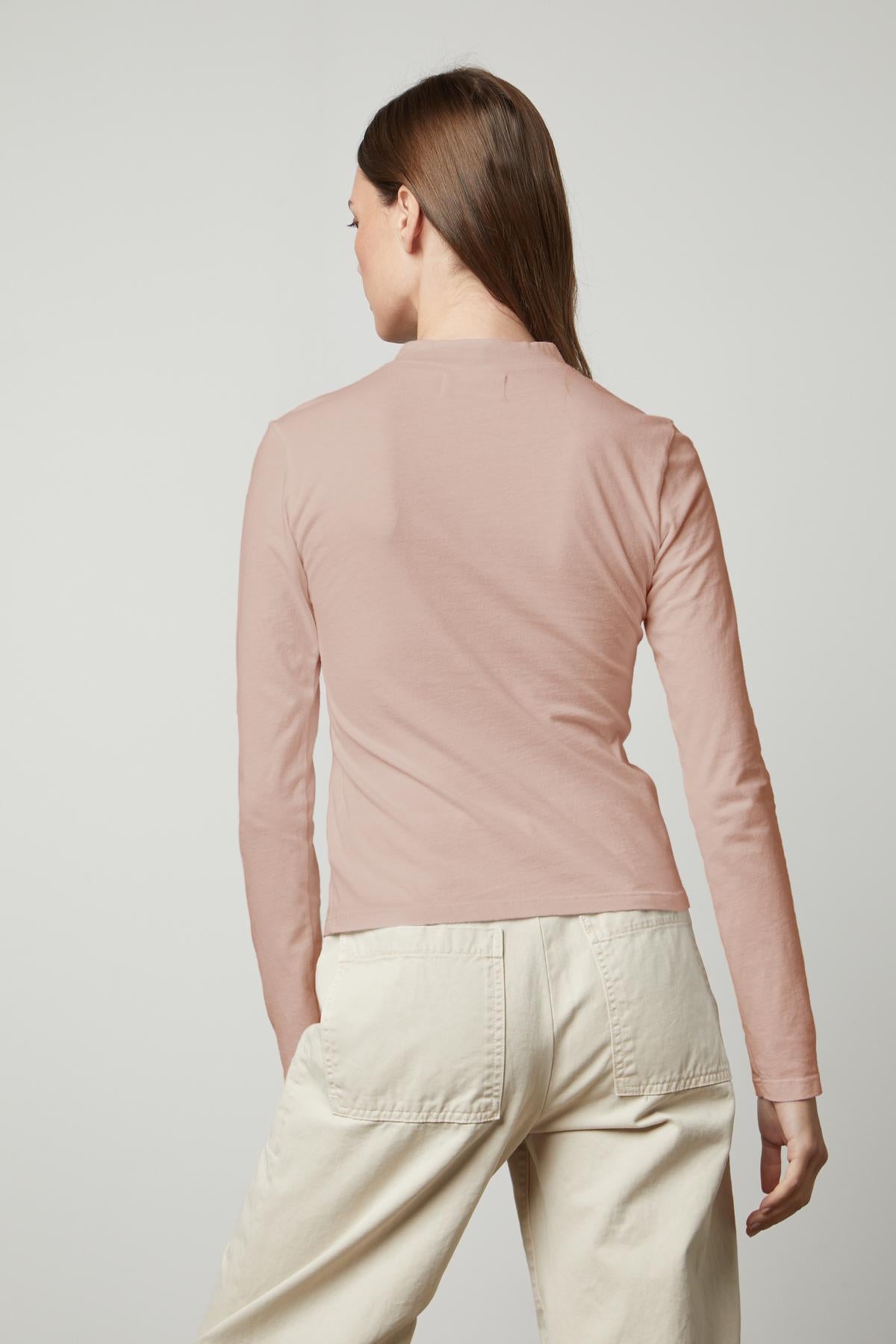 The silhouette of a woman in a Velvet by Graham & Spencer LINNY MOCK NECK TEE and white pants.-35660506792129