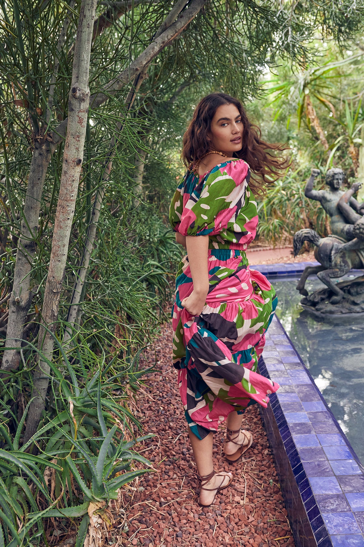 A woman in a floral dress, the Velvet by Graham & Spencer LYDIA PRINTED TIERED SKIRT, standing next to a fountain.-26342680985793