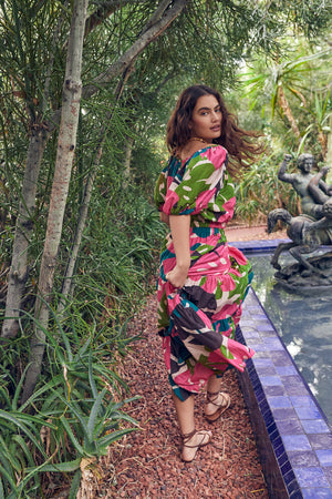A woman in a floral dress, the Velvet by Graham & Spencer LYDIA PRINTED TIERED SKIRT, standing next to a fountain.