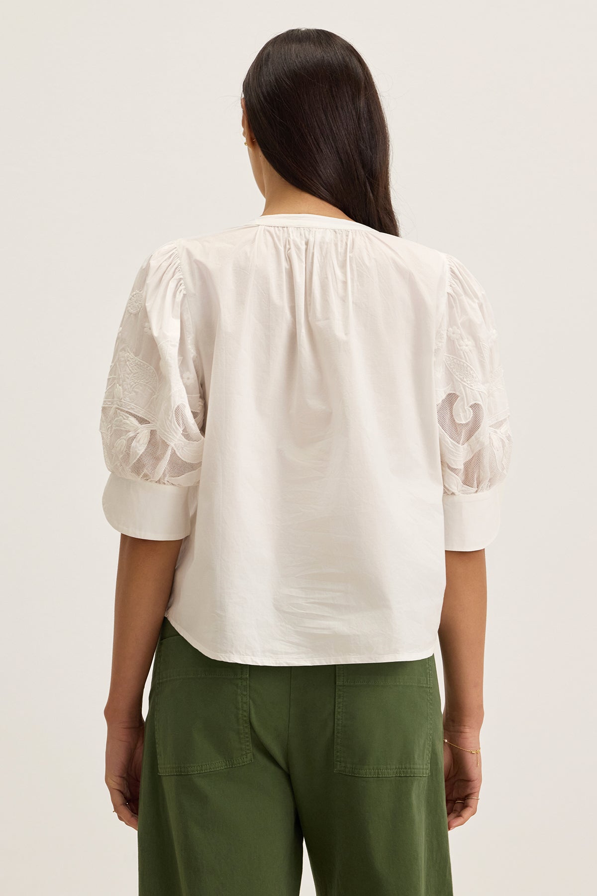 A woman is shown from the back wearing the LARIA TOP by Velvet by Graham & Spencer, a white cotton poplin blouse with sheer puff sleeves, paired with green pants against a plain light background.-39333154390209
