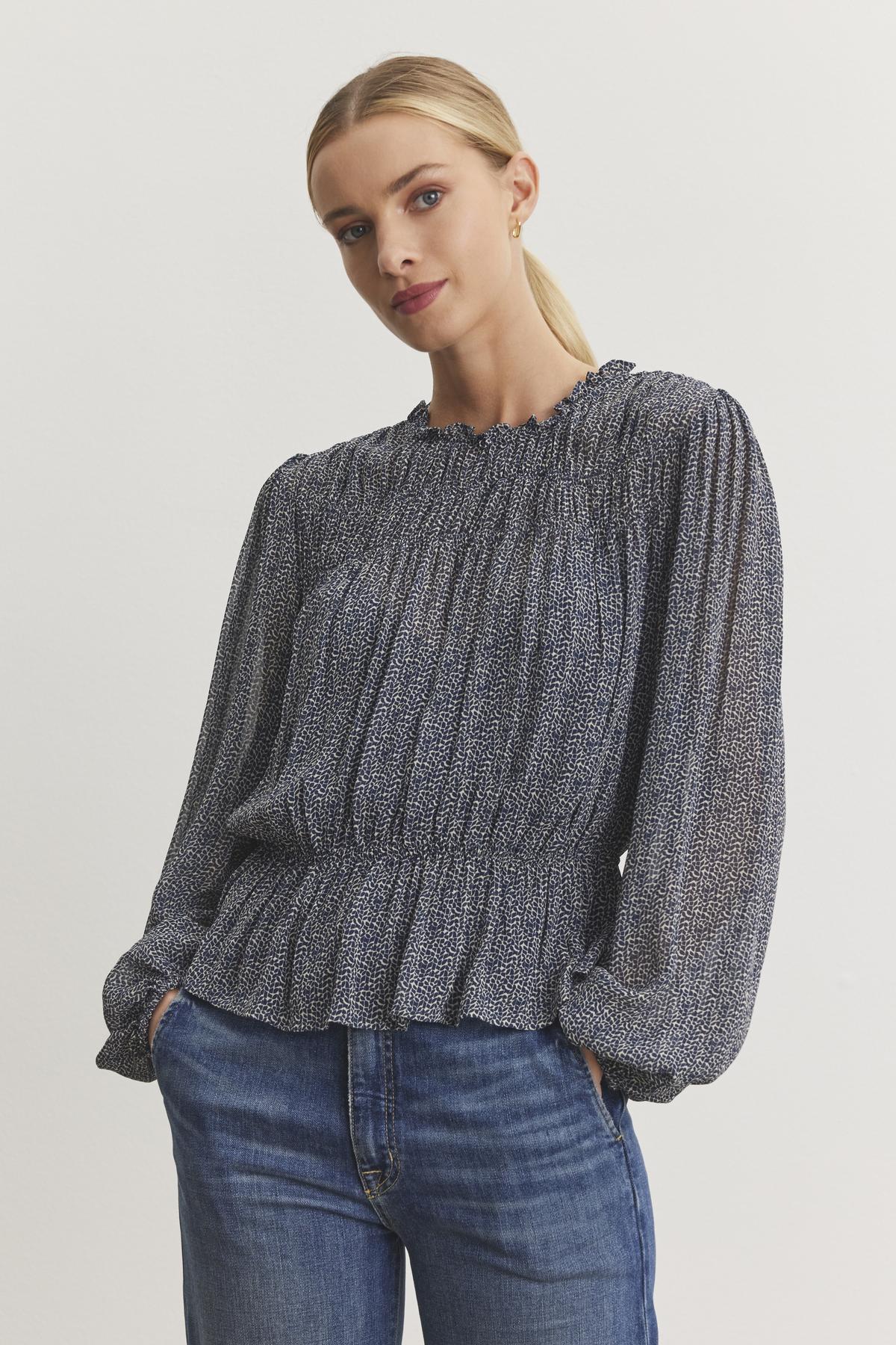 A woman wearing the BLEN TOP by Velvet by Graham & Spencer, featuring a ruffle neckline and a patterned design, paired with blue jeans, her hands casually resting in her pockets.-38246328336577