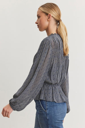 Side profile of a person with blonde hair in a ponytail, wearing the BLEN TOP from Velvet by Graham & Spencer paired with jeans, set against a plain background.