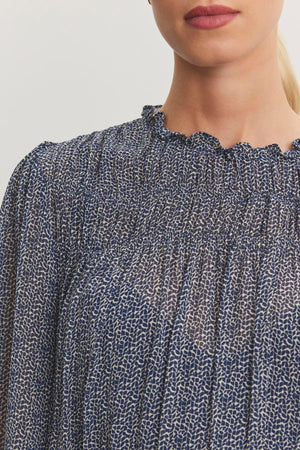 A close-up of a person wearing the Velvet by Graham & Spencer BLEN TOP, featuring a blue and white pattern with a smocked elastic and ruffled neckline.