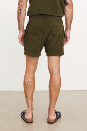 Rear view of a man wearing Velvet by Graham & Spencer's Salem shorts and brown loafers, standing with hands slightly behind him, highlighting visible tattoos on his arms and legs.