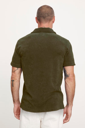 Rear view of a man in a Velvet by Graham & Spencer Sergey polo shirt and white pants, showing a tattoo on his left arm.