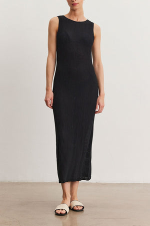 A woman stands in a neutral pose wearing a Velvet by Graham & Spencer Callen Dress, black and ribbed, paired with open-toed flat sandals, against a plain light background.