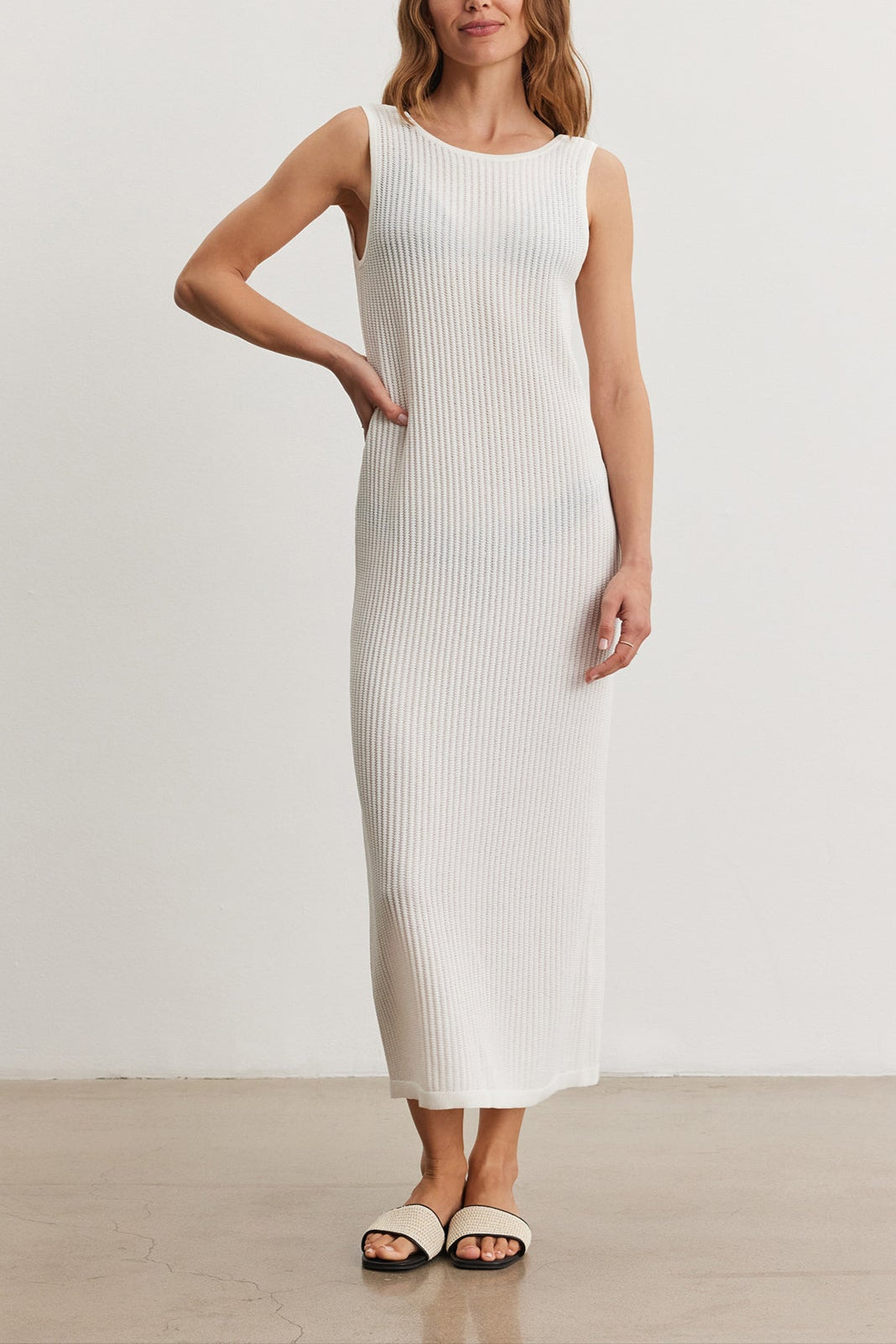 Woman in a white CALLEN DRESS by Velvet by Graham & Spencer standing with one hand on her hip in a bright, minimalistic room.-36909558890689