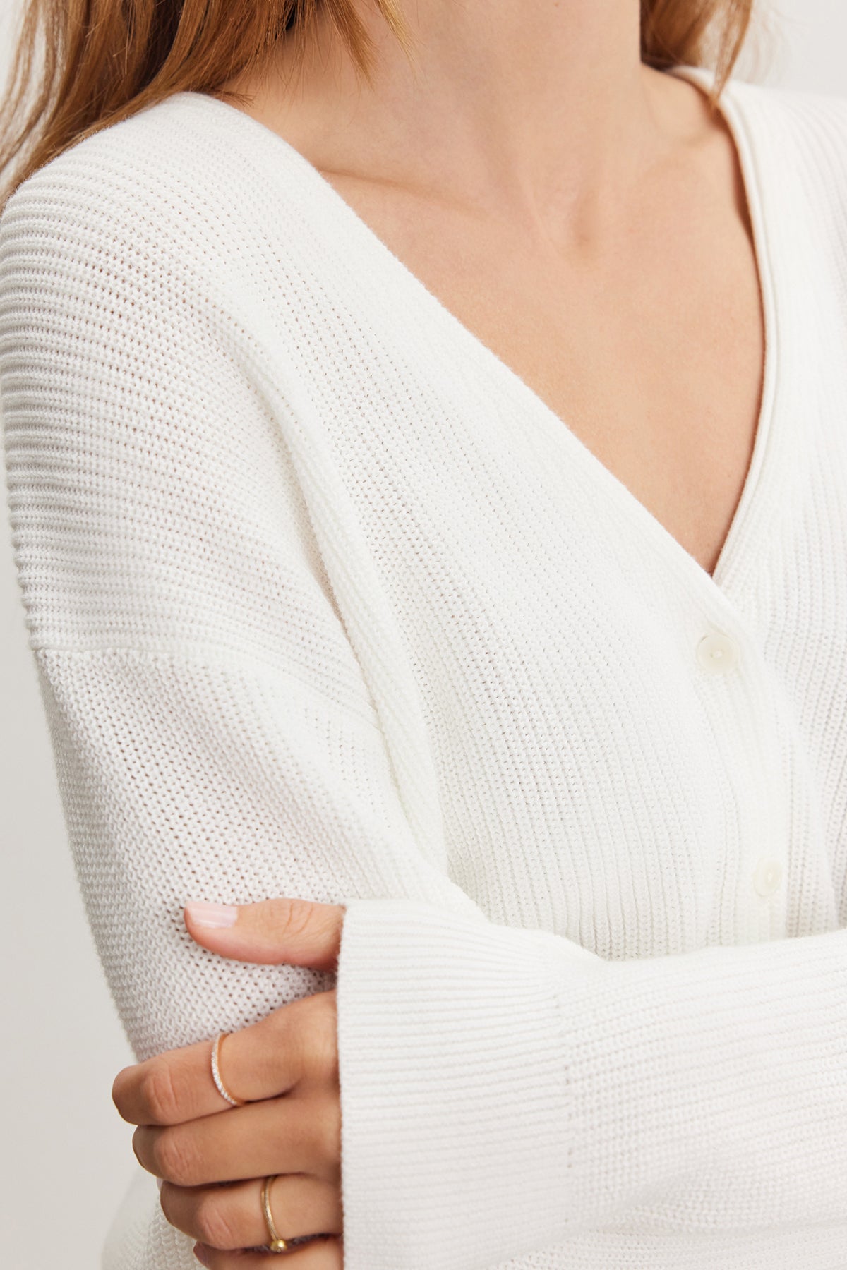 Close-up of a woman in a Velvet by Graham & Spencer Tava cardigan, focusing on the textured cotton knit fabric and her crossed arms with a visible gold ring on her finger.-36909564428481