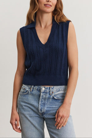 A woman wearing a navy blue WENDY SWEATER VEST and light blue jeans stands against a neutral background. Brand: Velvet by Graham & Spencer