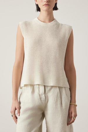 A person with short dark hair wearing the GARDENA LINEN SWEATER VEST by Velvet by Jenny Graham and relaxed fit, breathable linen pants stands against a plain background.