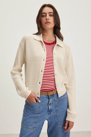 A person wearing a TAJ CARDIGAN by Velvet by Graham & Spencer over a red and white striped shirt with blue jeans and a brown belt stands against a plain background.