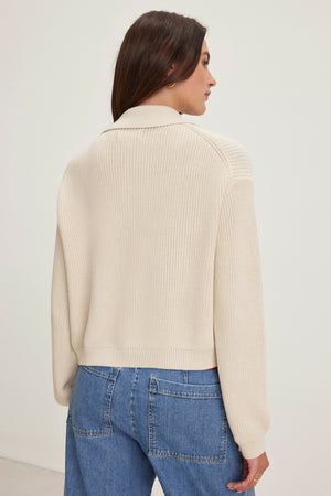 A person with long brown hair is wearing a Velvet by Graham & Spencer TAJ CARDIGAN in cream, made from textured cotton, paired with blue jeans, and is facing away from the camera.
