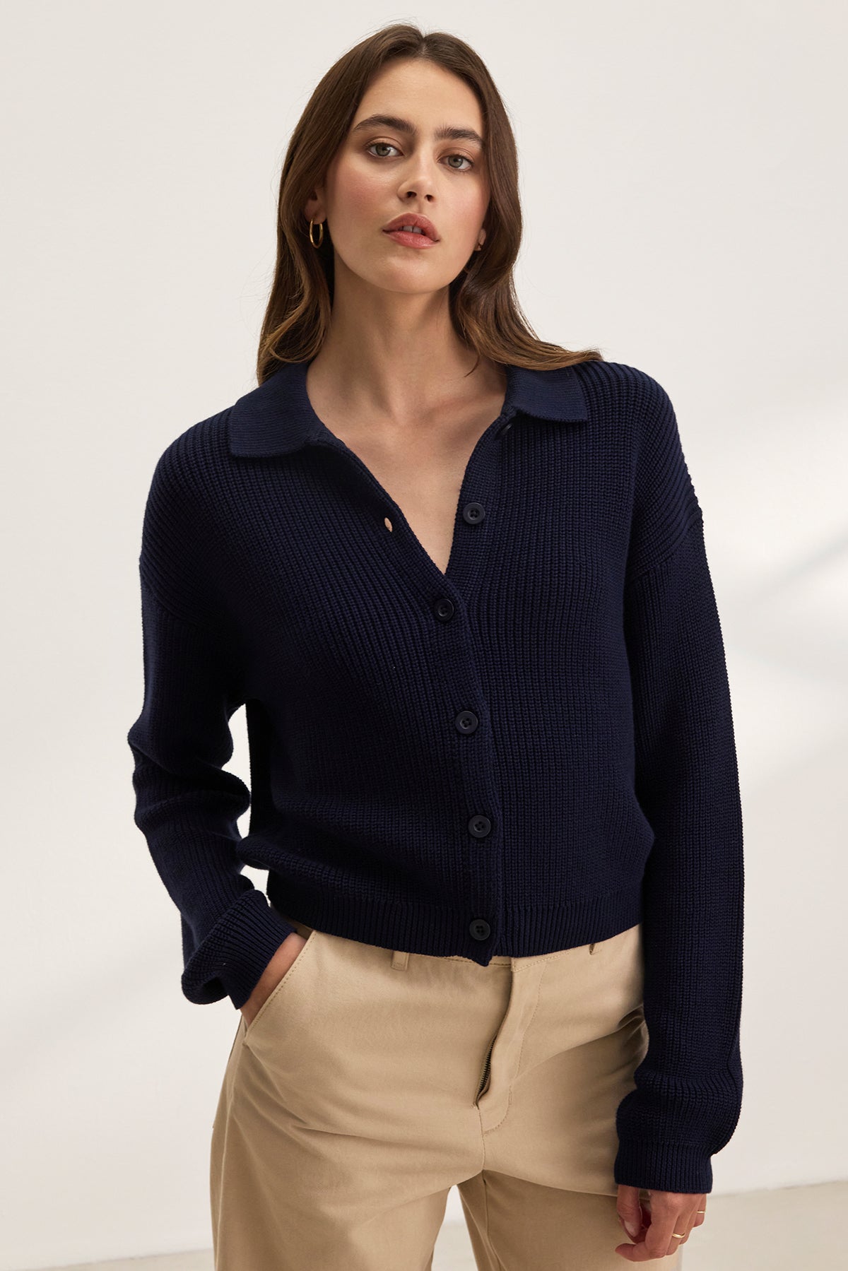 A woman wearing the TAJ CARDIGAN from Velvet by Graham & Spencer, a dark textured cotton cropped piece, with beige pants stands against a plain background.-38663164100801