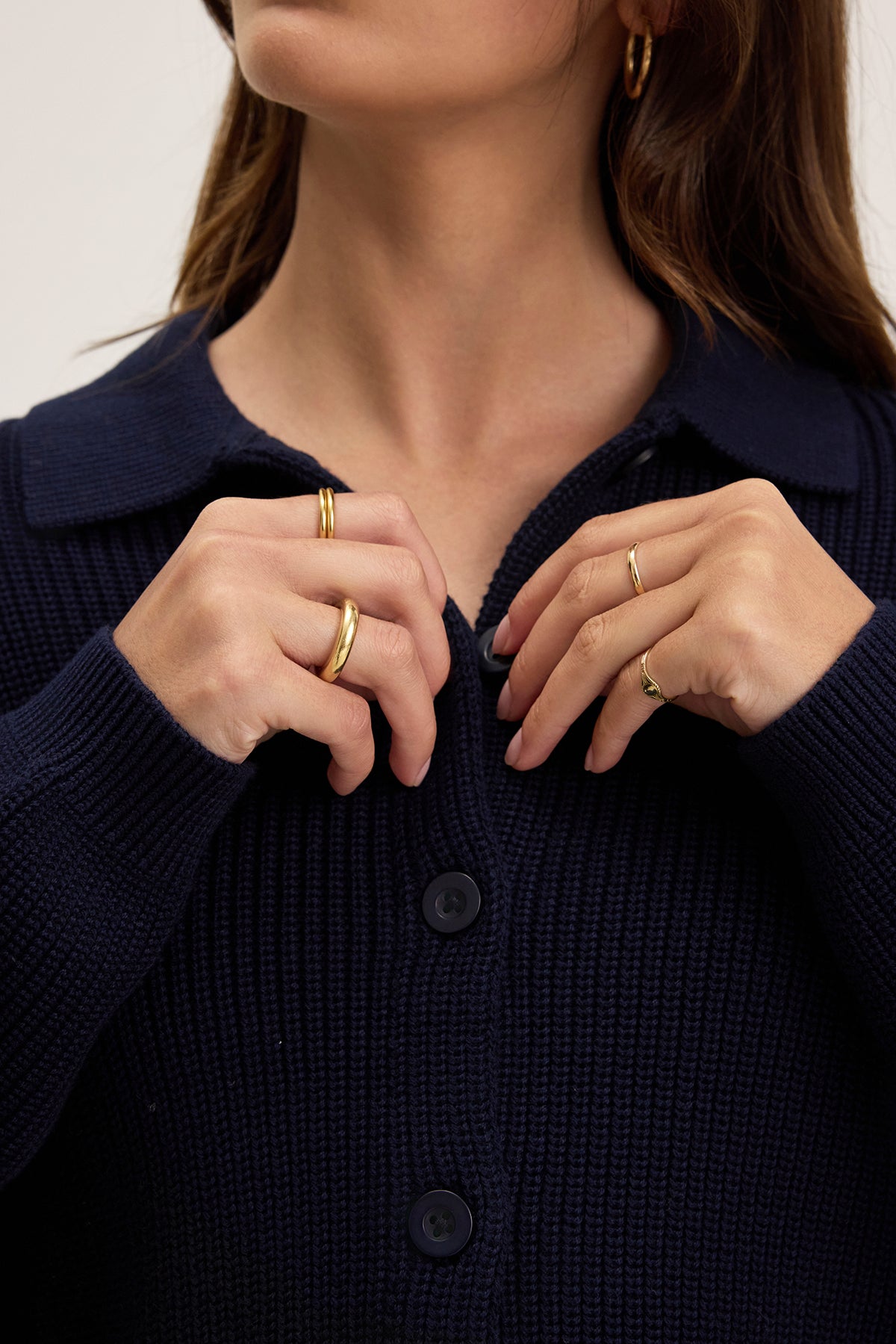 A person, adjusting the collar of a Velvet by Graham & Spencer TAJ CARDIGAN in textured cotton dark blue, adorned with gold rings on their fingers.
