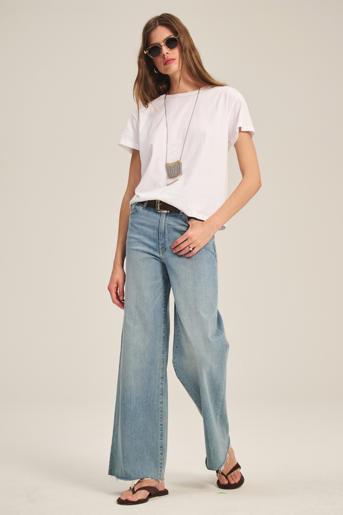 Wearing sunglasses, wide-leg jeans, a necklace, and sandals, a person models the TIA TEE by Velvet by Graham & Spencer against a plain background.-40305565827265