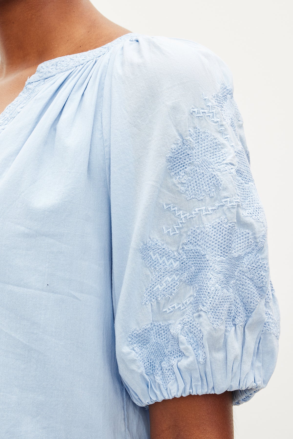 Close-up of a person wearing the CHRISSY DRESS by Velvet by Graham & Spencer, featuring intricate floral embroidery on the short, puffed sleeves that beautifully complement its v-neckline.