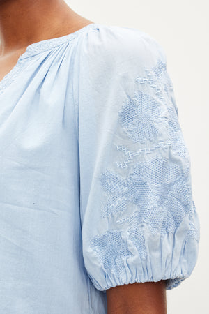 Close-up of a person wearing the CHRISSY DRESS by Velvet by Graham & Spencer, featuring intricate floral embroidery on the short, puffed sleeves that beautifully complement its v-neckline.