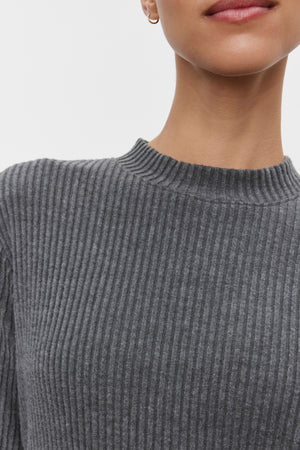 A close-up of a person wearing the LIZ Ribbed Dress by Velvet by Graham & Spencer, characterized by its grey ribbed texture and crew neckline. The lower half of the face is visible, showcasing neutral lips.