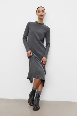 A person poses in a knee-length, long-sleeved LIZ RIBBED DRESS by Velvet by Graham & Spencer with a crew neckline and black ankle boots, standing against a white wall.