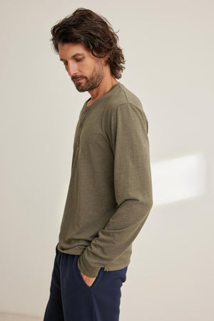 A person wearing a Velvet by Graham & Spencer DESI HENLEY in green with dark pants stands against a light background.