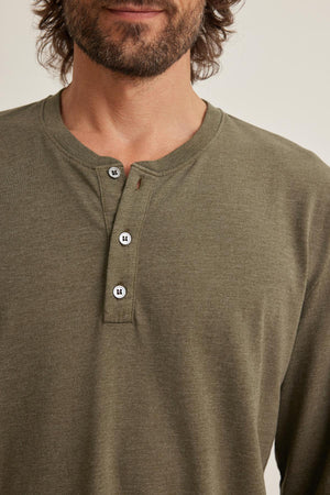 A person wearing the Velvet by Graham & Spencer DESI HENLEY in green, featuring three visible buttons, stands against a plain background.