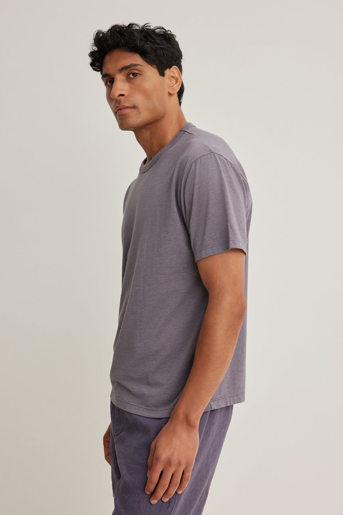 A man stands sideways against a plain light background, wearing the Velvet by Graham & Spencer ZANDER TEE, a relaxed fit short-sleeved gray t-shirt, paired with matching gray pants.