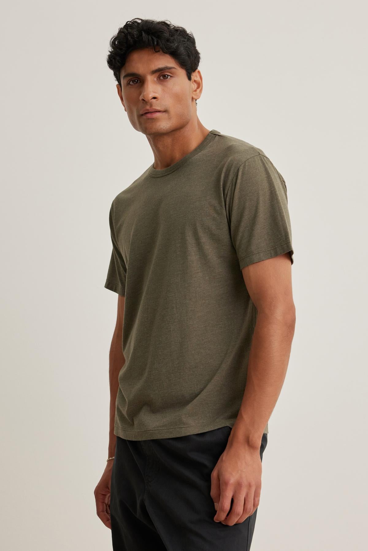 Someone wearing the ZANDER TEE by Velvet by Graham & Spencer and black pants is standing against a neutral background.