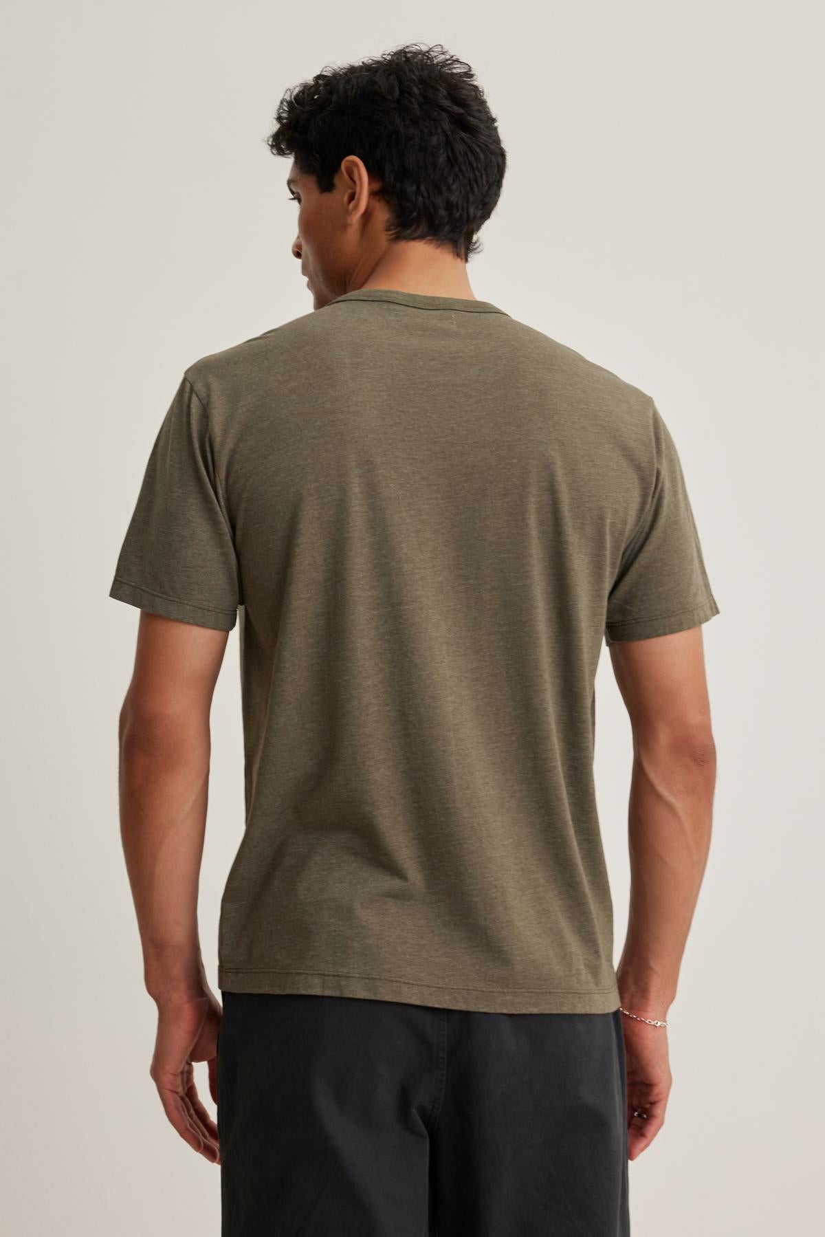 Someone with short curly hair models the Velvet by Graham & Spencer ZANDER TEE, paired with dark shorts, standing with their back to the camera against a plain background.