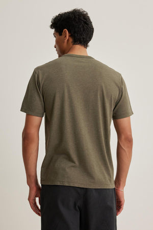 Someone with short curly hair models the Velvet by Graham & Spencer ZANDER TEE, paired with dark shorts, standing with their back to the camera against a plain background.