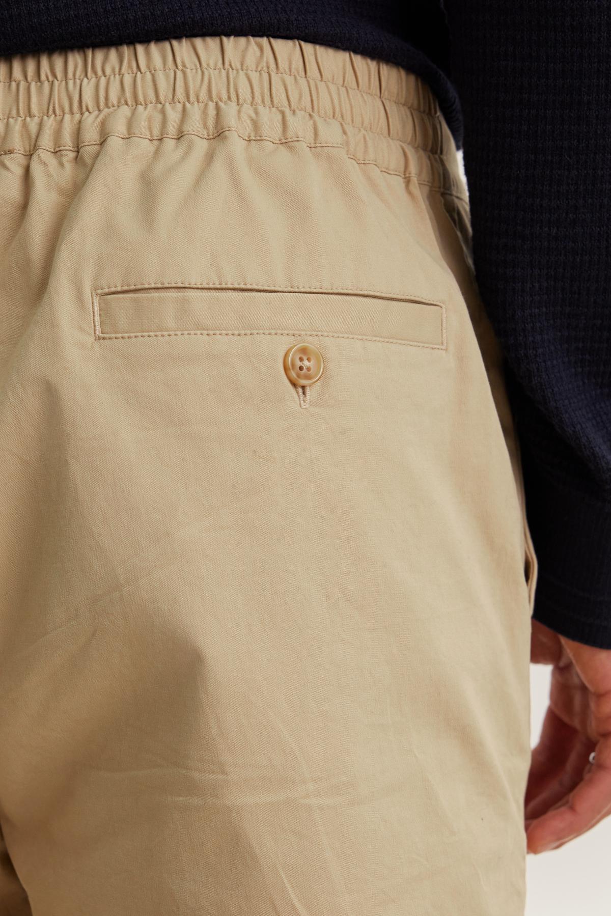 Close-up of someone in Velvet by Graham & Spencer's STONE PANT, featuring an elastic waistband and buttoned back pocket, paired with a dark long-sleeve top.-38643359416513
