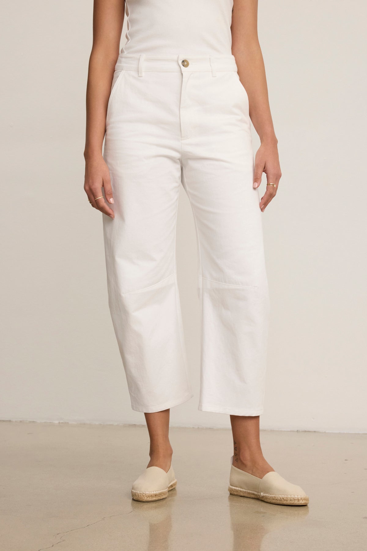 A person wearing a sleeveless white top, Velvet by Graham & Spencer ALEXIS PANT in white cotton twill with knee darting, and beige espadrille shoes stands against a plain background.-39119701475521